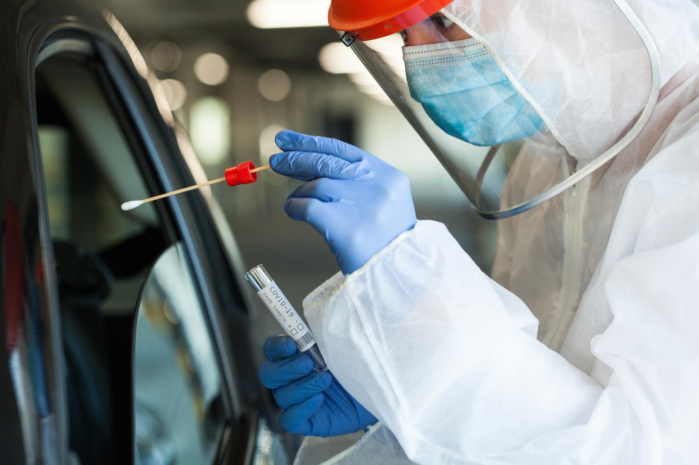 A person wearing protective equipment administering a drive through COVID-10 test.