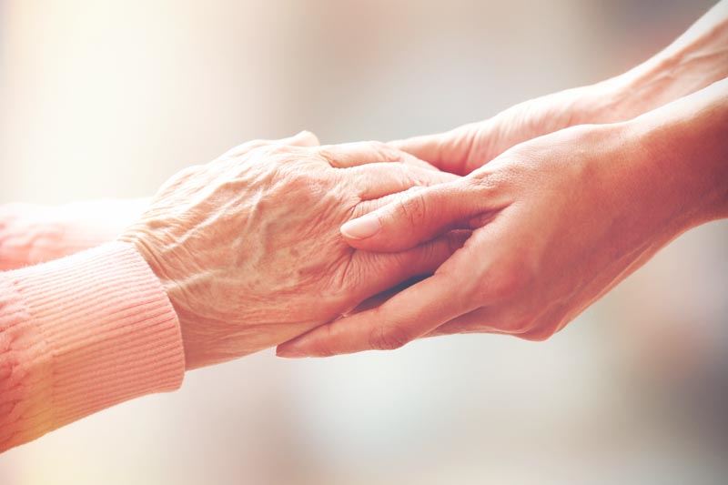 A younger person holding the hands of an older person.