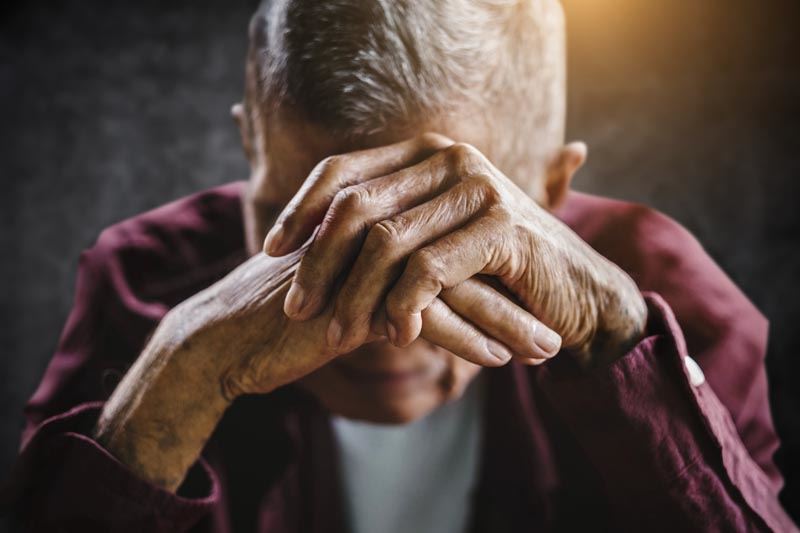 An elderly man resting his head on his hands.