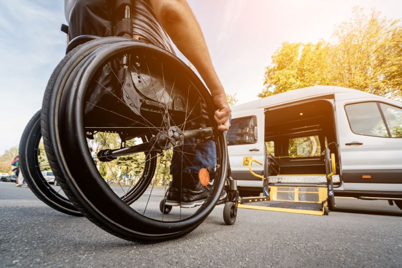 A person in a wheelchair next to a van with a wheelchair lift.